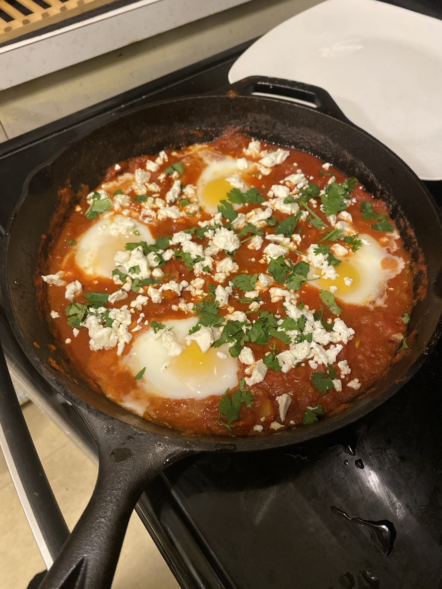 Cast-iron skillet of shakshuka — eggs poached in tomato sauce, topped with feta and cilantro