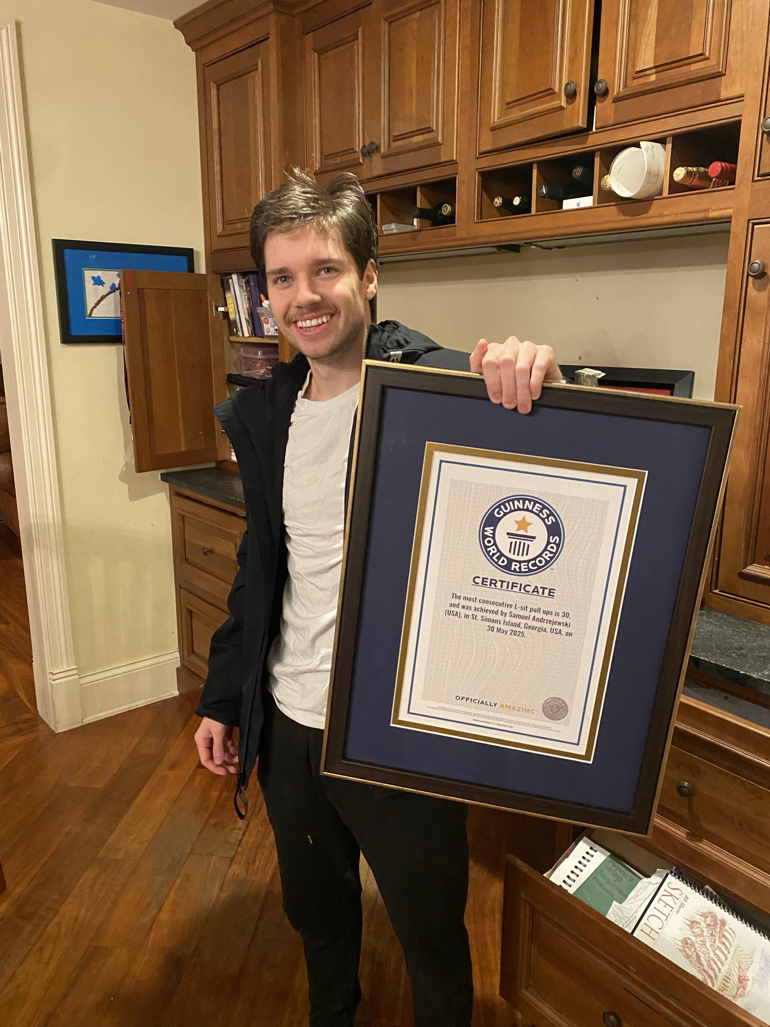 Sam holding a framed Guinness World Records certificate for the most consecutive L-sit pull-ups, 30
